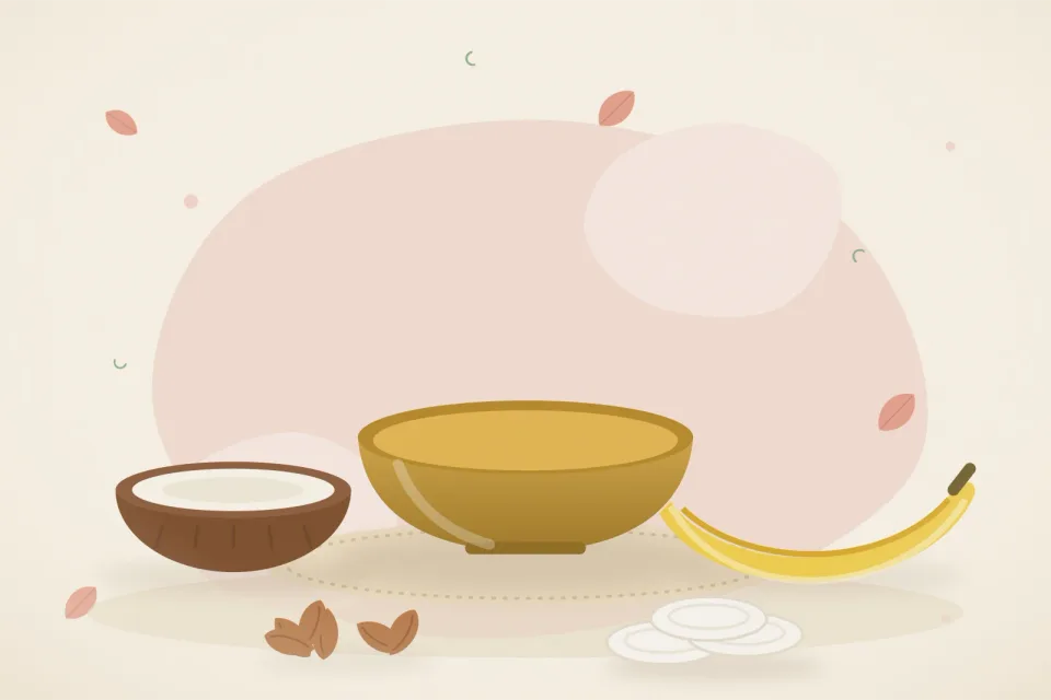 A small bowl of warm oil, half a coconut, almonds, a banana and cotton pads on a rose-pink background
