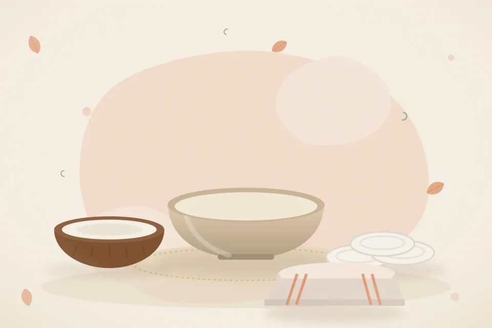 Half coconut with a small bowl of coconut oil, cotton pads and a soft folded cloth on a peach background