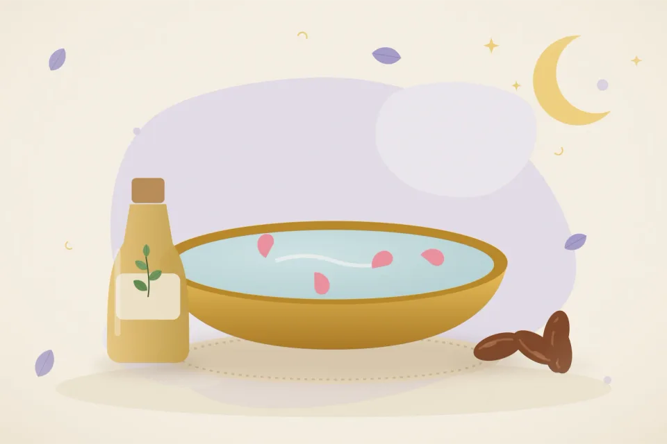 Brass basin of warm water with rose petals, a bottle of sesame oil and a bowl of dates on a lavender background
