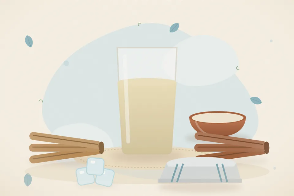 A small piece of mulethi and a cinnamon stick beside a cup of pale warm infusion on a wooden table.
