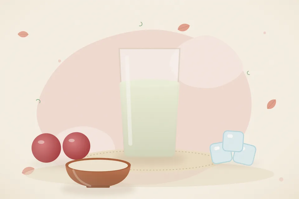 A small glass of deep red pomegranate juice beside a cut pomegranate and loose ruby arils on a wooden board.