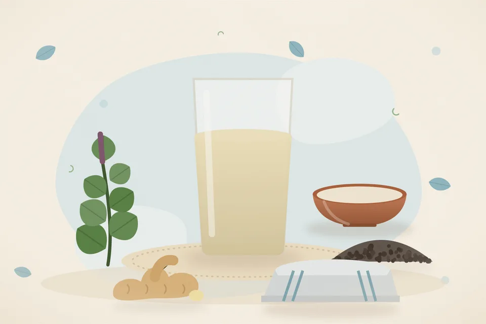 A steel cup of tulsi and pepper kadha on a stove ledge, with tulsi sprigs, two peppercorns, and a slice of ginger nearby.